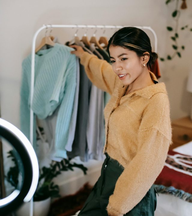 Young woman recording fashion content indoors with a smartphone and ring light.